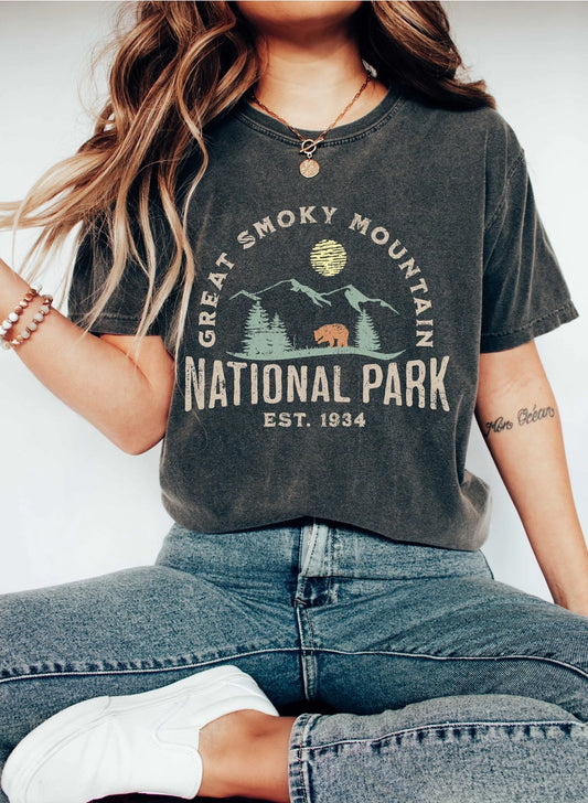 Girl sitting down in a dark gray t-shirt with Great Smoky Mountain National Park printed on it as well as a graphic image of mountains, the moon, and a bear.