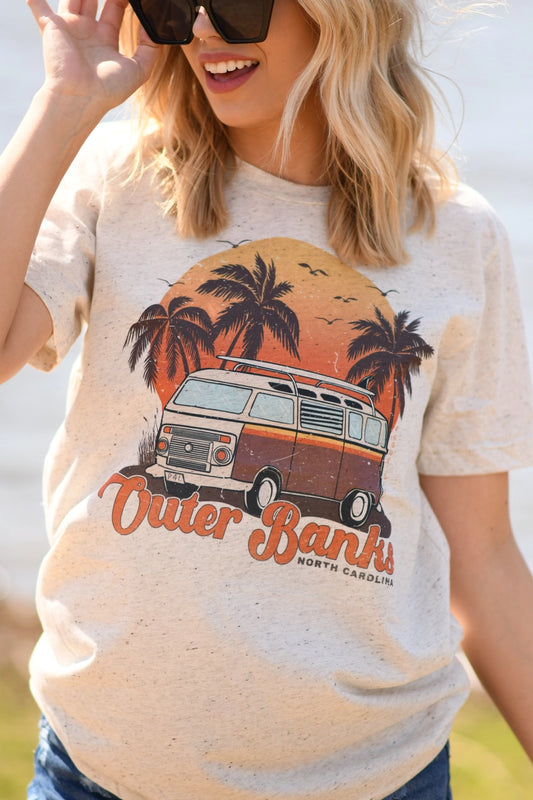 A girl in a cream colored t-shirt with a retro van, palm trees, sun and Outer Banks North Carolina printed on it.