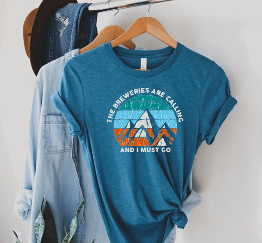 A heather teal blue t-shirt with the words The Breweries are Calling And I Must Go printed on it along with graphic mountains with green, light blue and orange design.